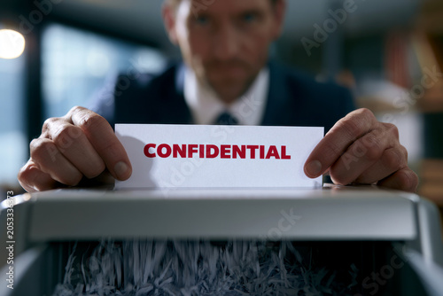 male office worker Putting Confidential Document Into Privacy Paper Shredder Machine Destroying Confidential Document File.