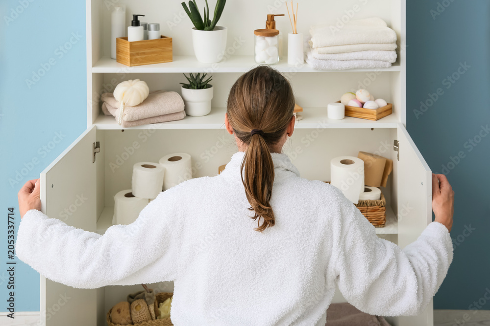 Obraz premium Woman in white robe organizing bathroom cabinet with toilet paper and personal care products, home organization and storage