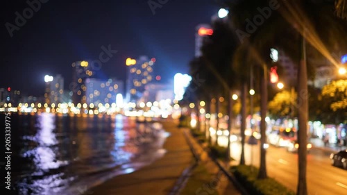 Blurred night city lights on coastal road with palm trees
