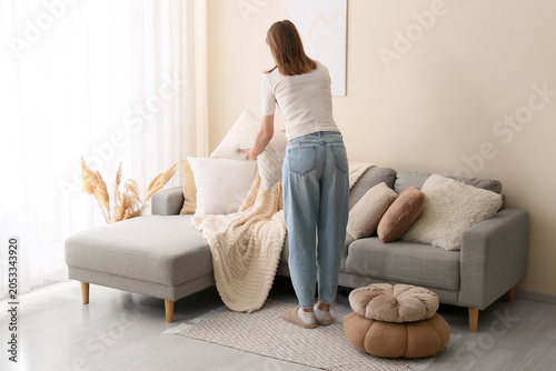 Photos Young woman arranging decorative pillows on a modern gray sofa in a bright livin