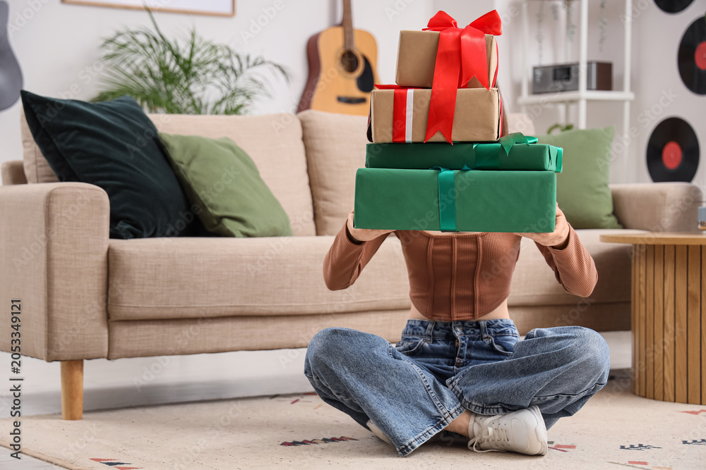 Fototapeta premium Young woman holding stack of wrapped holiday gifts, celebration and surprise, festive occasion, home interior