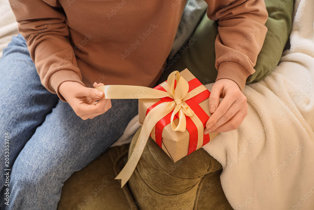 Fototapeta premium Person tying golden ribbon on brown gift box with red ribbon, holiday celebration and special occasion present, this activity represents the joy of holiday celebrations and special occasions