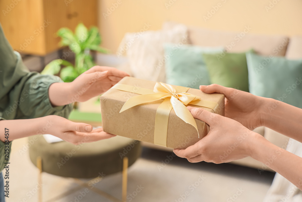 Fototapeta premium Hands exchanging gift box wrapped in brown paper with gold ribbon, present giving and receiving