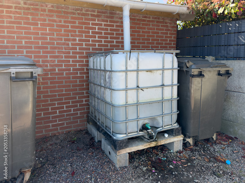Rainwater harvesting tank beside brick wall and trash bins