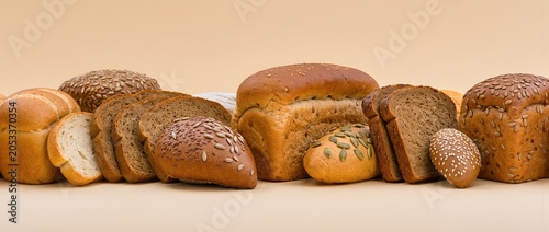 Group of diverse fresh bread loaves buns and slices stacked together on beige surface panoramic front view