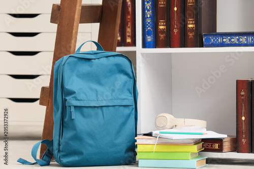 Blue backpack with school supplies and bookshelf in a modern study room setti...