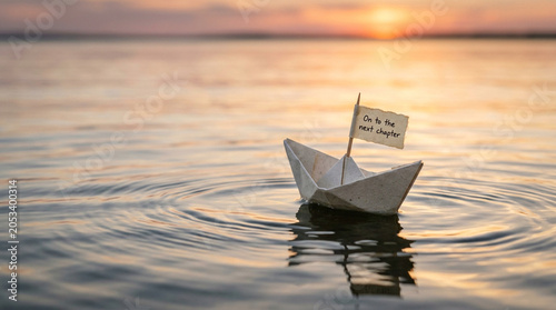 Paper boat floating on calm water at sunset, origami ship with On to the next chapter flag, metaphorical journey and new beginnings concept