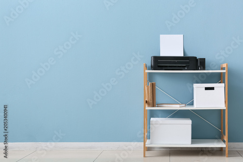 Принти на полотні Home office printer and storage shelf with books and boxes against a blue wall b