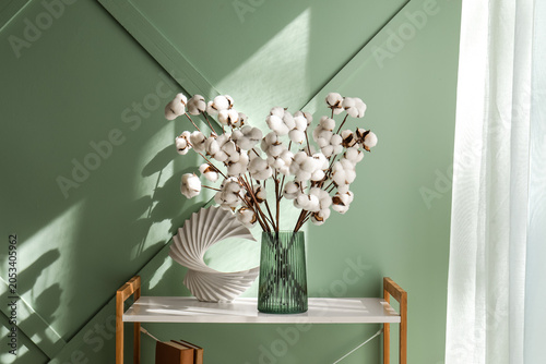 Quadro su tela Fluffy white cotton bolls in green ribbed vase on white shelf with books and mod