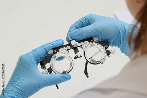 Obraz na plátně Optometrist hands in blue gloves adjusting phoropter for vision test and eye exa