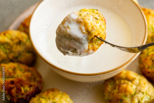 Bild auf Leinwand Close-up of a golden crispy baked zucchini tot being dipped into a small bowl of