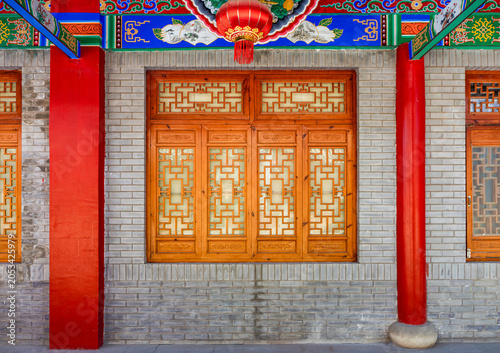 Traditional Chinese Architecture with Red Pillars and Wooden Lattice Windows. Traditional Chinese building facade with ornate wooden lattice windows, red support pillars, hanging lantern, brick wall.