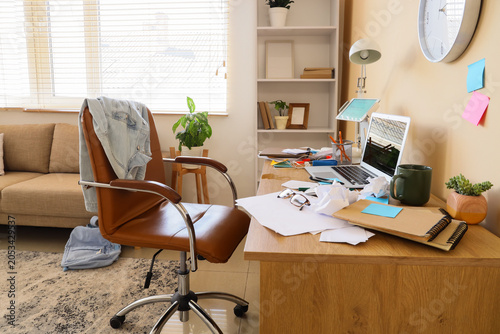 Billede på lærred Messy home office desk with laptop, papers, and chair, remote work environment,