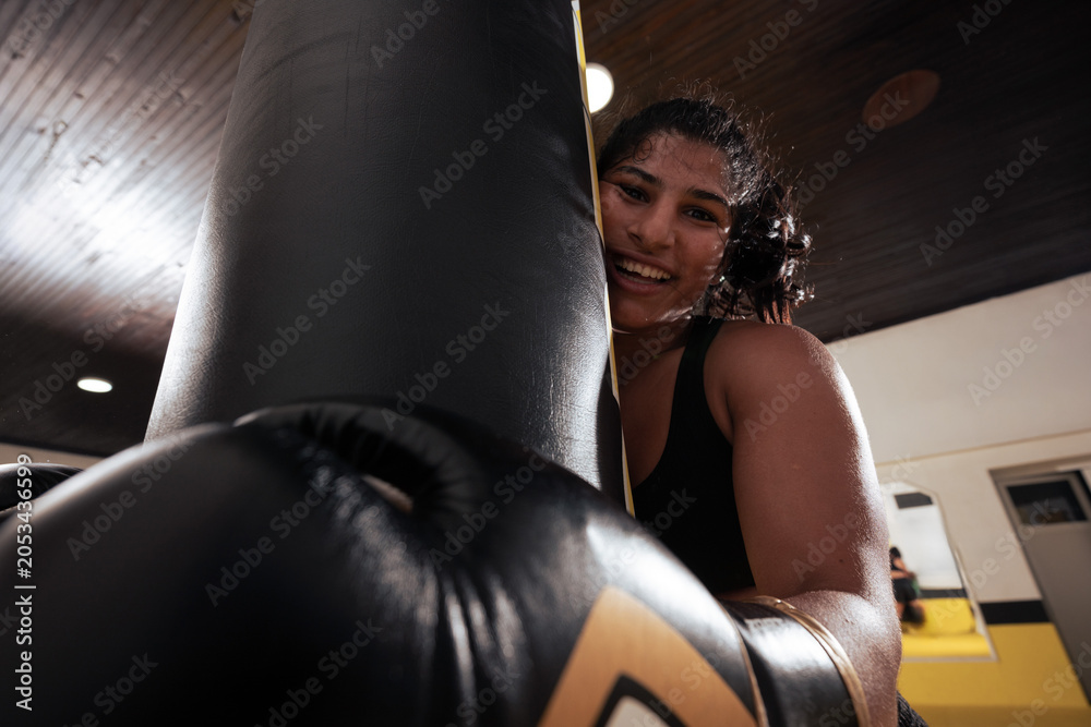 Naklejka premium Young Woman Boxing With Punching Bag in Gym Smiling During Fitness Training Session