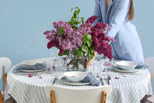 фотографія Woman arranging fresh lilac flowers in vase on dining table with place settings