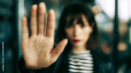 Young woman showing a stop gesture, rejection with her raised hand while looking directly at the camera with a serious facial expression in this cinematic blurred portrait