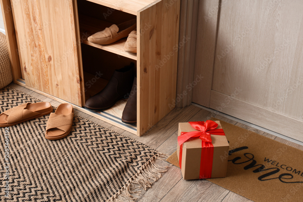 Fototapeta premium Home entryway with wooden shoe cabinet, welcome mat, and gift box, organized modern interior design
