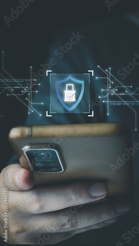 A person holds a smartphone displaying a virtual holographic security shield with a padlock and circuit lines, illustrating futuristic cybersecurity concepts.