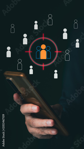 A person uses a smartphone displaying a virtual interface with a red crosshair targeting a specific group of user icons, illustrating audience segmentation.