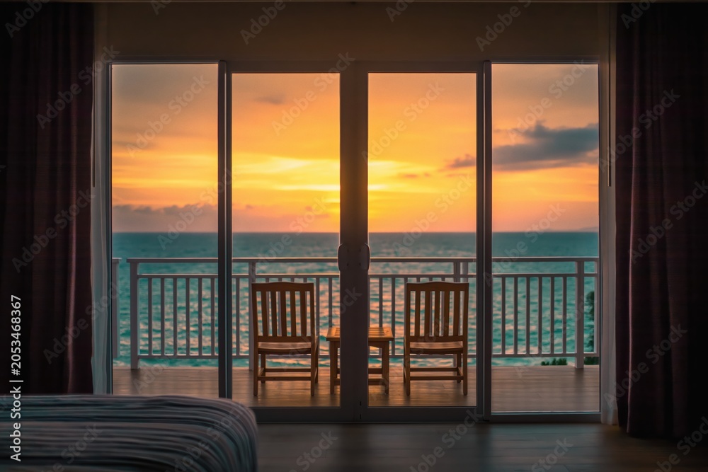 Fototapeta premium Sunset ocean view from hotel balcony with chairs, tropical vacation resort room window
