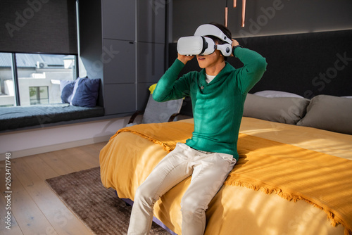White VR headset with headphones is resting on edge of mustard bed near window seat