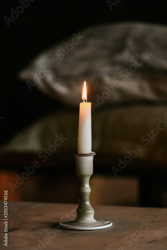A single white lit candle in a ceramic holder casting a warm glow against a dark, rustic background.