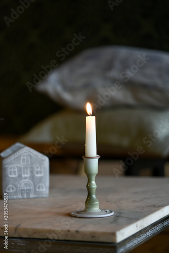 A single white lit candle in a ceramic holder casting a warm glow against a dark, rustic background.