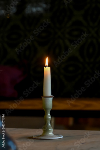 A single white lit candle in a ceramic holder casting a warm glow against a dark, rustic background.