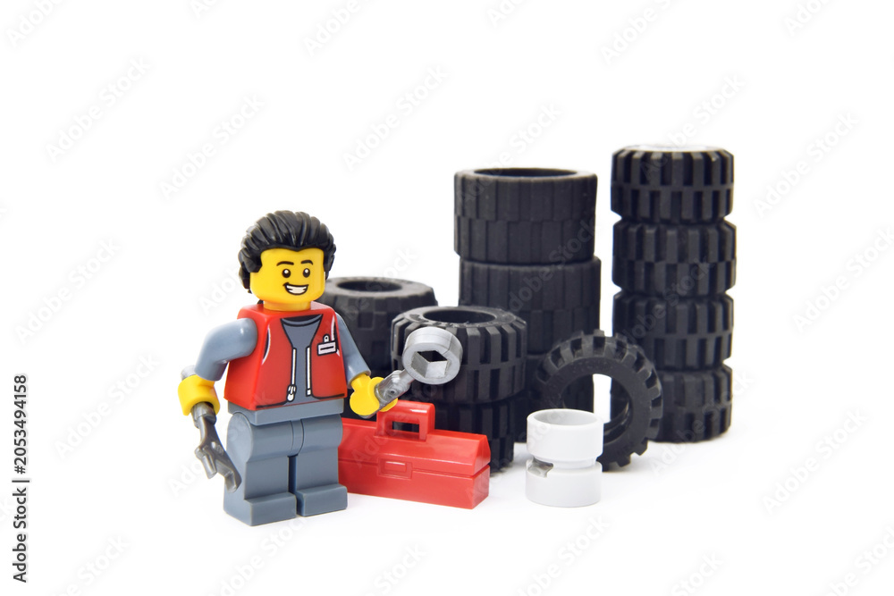 Naklejka premium Editorial illustrative image of lego minifugure of mechanic with tires in car service of repair isolated on white. Popular children toy of plastic bricks constructor.
