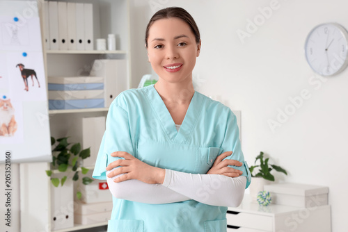 Smiling female veterinarian in scrubs with folded arms in modern animal clini...