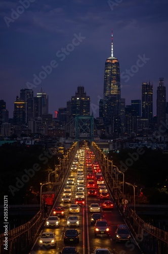 Busy city traffic on a bridge at night with glowing car headlights and a tall skyscraper silhouette in the background