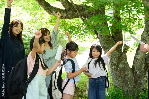 新緑の木の下で先生と一緒に右手を挙げて気合いを入れる親子と女子小学生たちのグループ