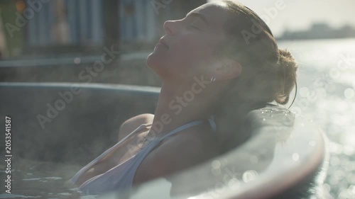 Spa calm surrounds the woman as she relaxes in a steaming hot tub by the water