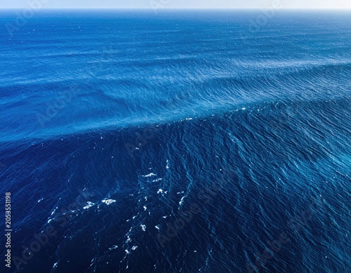 Aerial view of the vast, textured ocean surface under a clear blue sky, capturing the interplay of light