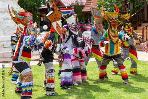 Performers in vibrant handcrafted ghost masks and patchwork outfits dance on green grass during the traditional Phi Ta Khon festival in Loei, Thailand.