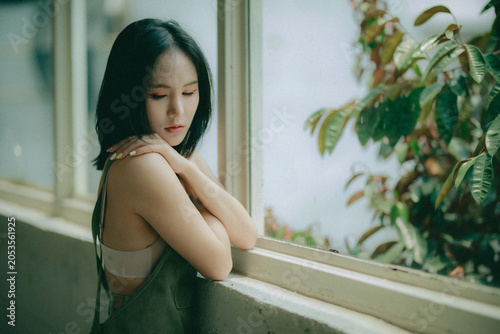 Fotografie Vulnerable woman sitting by a glass window, her facial expression capturing the agonizing pain of mental illness
