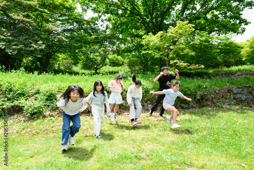新緑の広場を元気よく走る複数人の小学生たち
