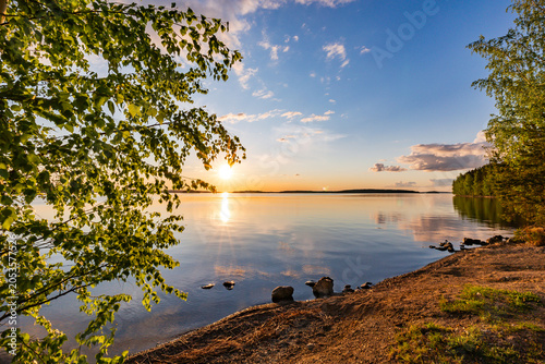 Scenic midsummer sunset over a calm lake in Finland with birch tree framing.