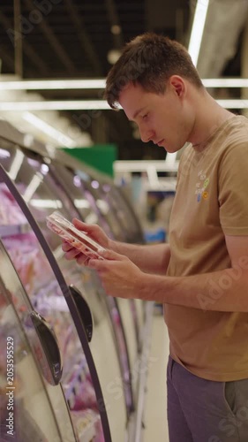 Young man selecting packaged meat from refrigerated supermarket display