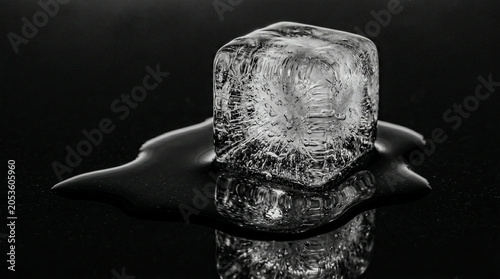 Melting ice cube trapped bubbles fractures glowing on jet black, mono macro