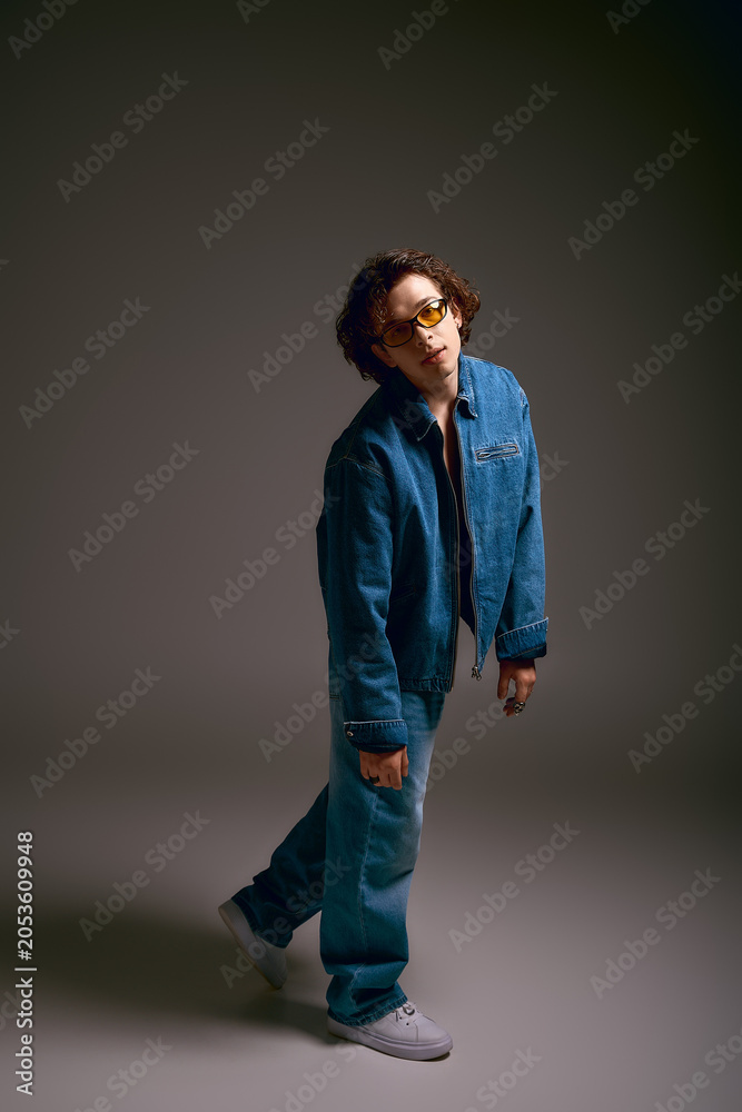 Fototapeta premium Emotional young man with curly hair dressed in stylish denim exudes artistic flair in studio setting