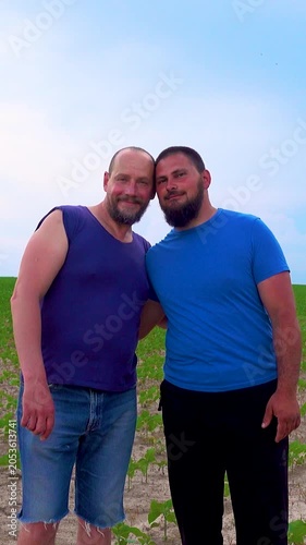 An emotional embrace of two handsome mature men walking in nature. A happy gay couple on a walk in a field, having a fun time. Vertical video.