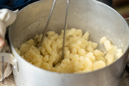 Obraz na płótnie Metal masher crushing boiled potatoes in a stainless steel pot, showcasing tradi