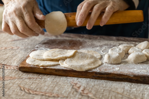 Cuadro en lienzo Close up of a person using a wooden rolling pin to flatten dough circles on a fl