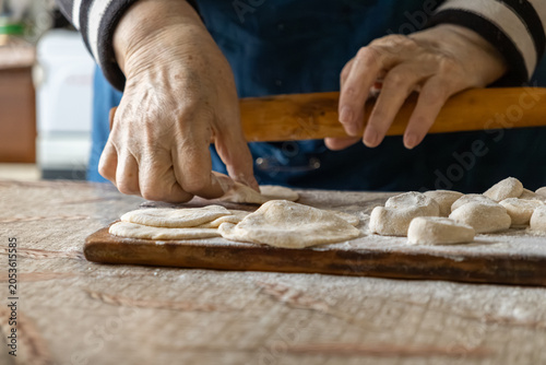 Fotografie An elderly person uses a wooden rolling pin to flatten dough on a floury board f