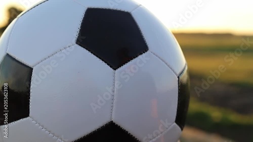 A close-up view of a classic black and white soccer ball rests on a vibrant green field during a beautiful golden sunset, building excitement for World Cup 2026 hosted by Canada and USA
