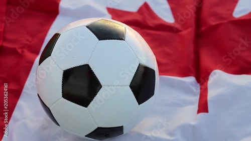 A classic black and white soccer ball rests on a waving Canadian flag, clearly representing Canada's role as a host nation for the upcoming  World Cup 2026 alongside the USA and Mexico