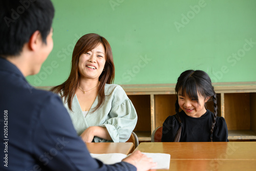 教室で先生と和やかに三者面談をする母親と女子小学生