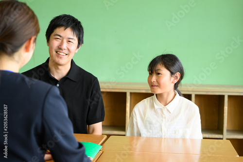 教室で先生と和やかに三者面談をする父親と高学年の女子小学生