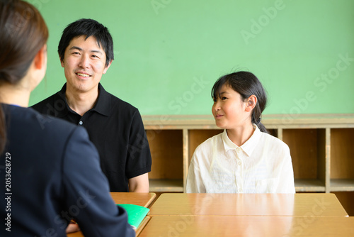 教室で先生と和やかに三者面談をする父親と高学年の女子小学生